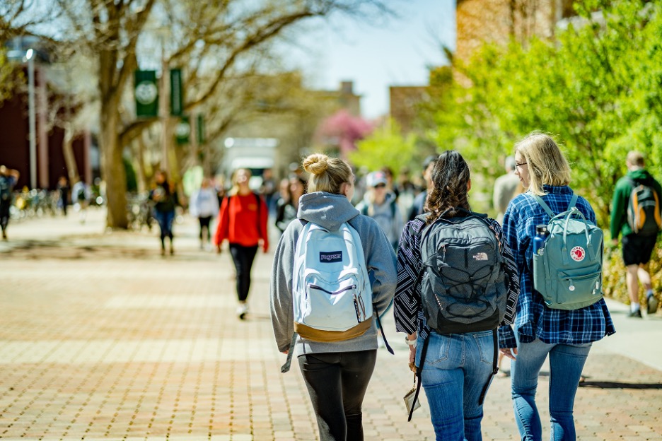 Students wearing backpacks walking on a college campus discussing Jurna